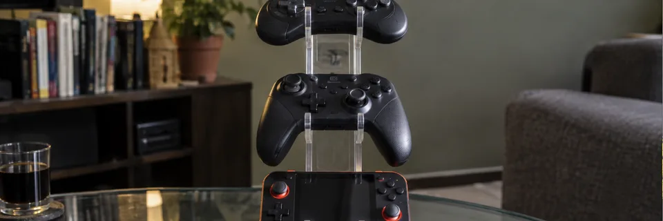 Controles 8BitDo e GameSir e console portátil retrô Anbernic num suporte de acrílico